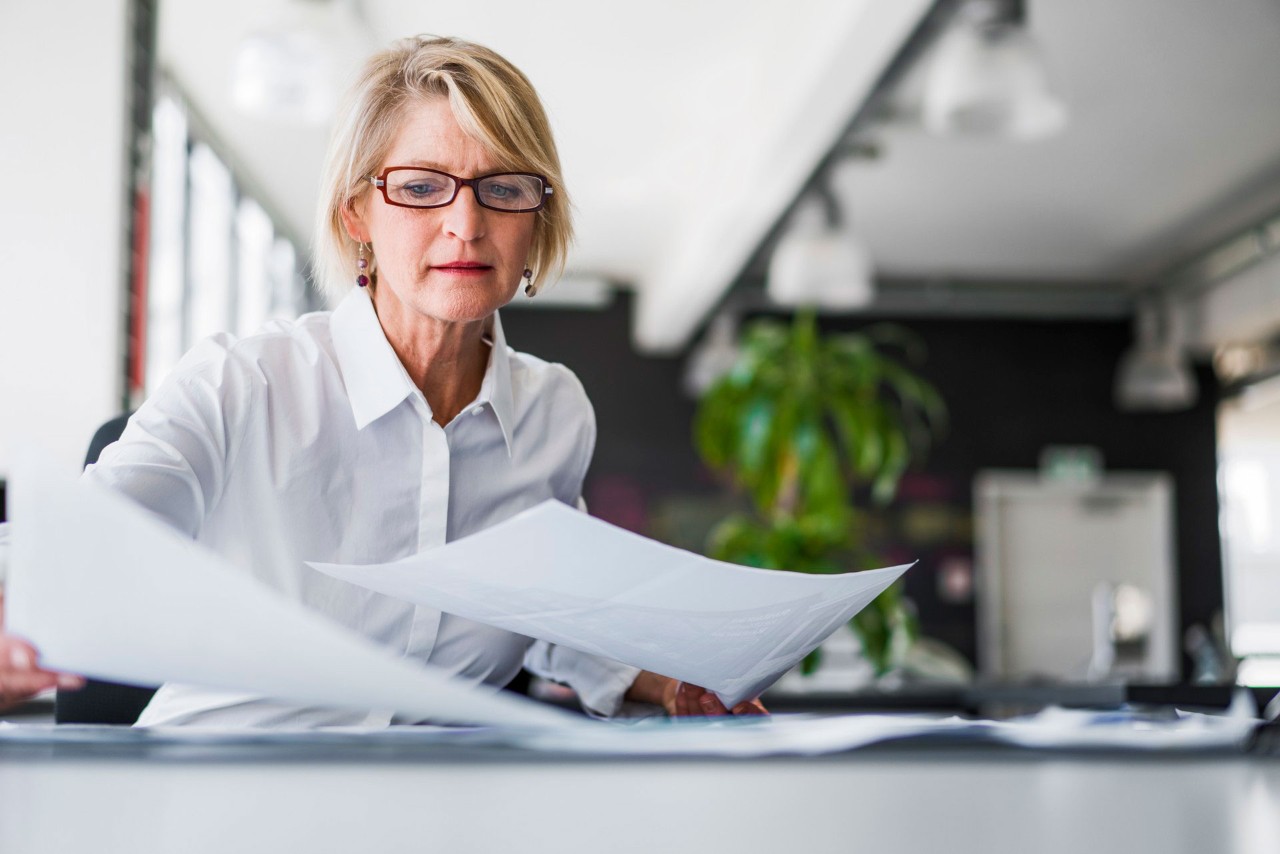 Women with blonde hair and brown glasses is looking down while sorting some papers.